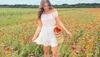 Woman in white sundress and white cowboy boots walking through field of flowers