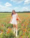 Woman in white sundress and white cowboy boots walking through field of flowers