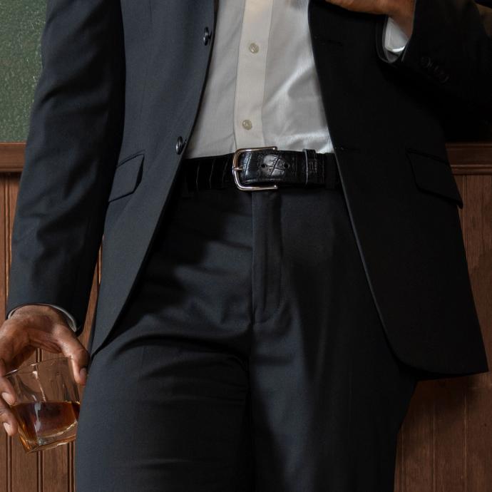 Close up of a man's waist who is wearing a suit and midnight colored crocodile belt