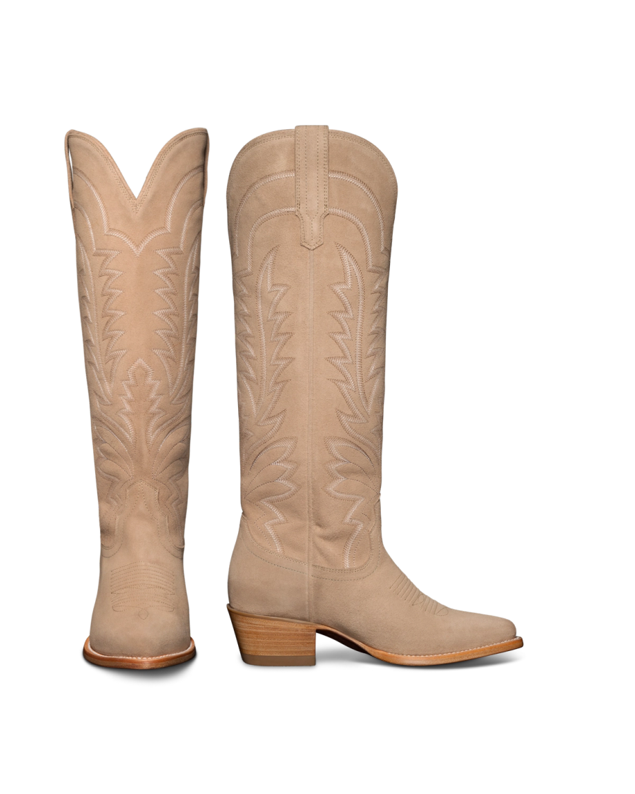 A pair of tall, tan cowboy boots with intricate stitching and wooden heels, displayed against a black background.