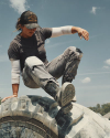 A person in work clothes and a hat sits on top of a large tractor tire outdoors under a partly cloudy sky.
