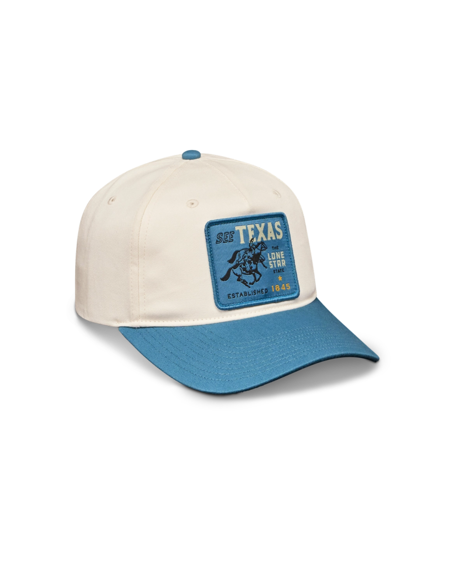 A cream-colored baseball cap with a blue brim and a blue patch reading "SEE TEXAS LONE STAR ESTABLISHED 1845" featuring an illustration of a bucking horse.