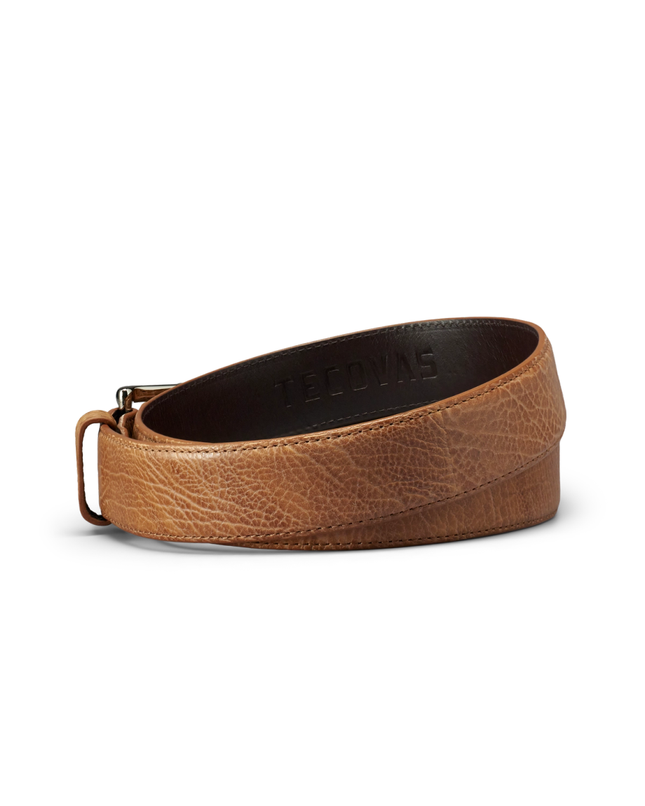 A brown leather belt with a suede finish, coiled and showing the embossed word "Tecovas" on the inner side.