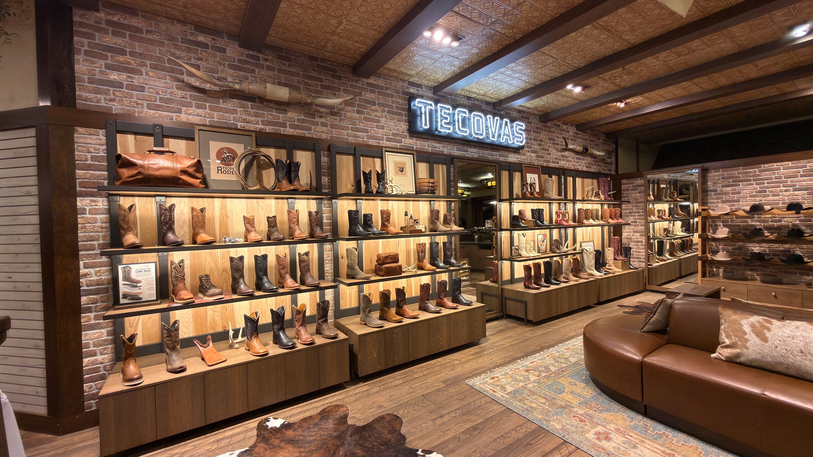 Interior of a Tecovas retail store featuring shelves of leather cowboy boots, a brick wall, and a neon sign with the brand name.