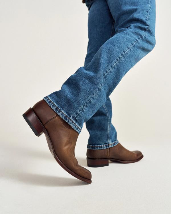 Person walking, wearing brown leather ankle boots and blue jeans against a plain background.