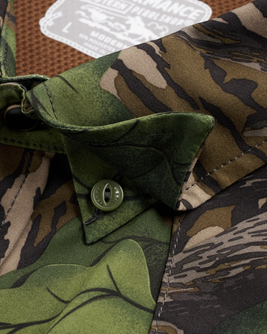 Close-up of a camouflage shirt collar with a green button, featuring mixed camo patterns in green, brown, and black, with a size label visible in the background.