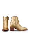 Two gold cowboy boots, one facing forward and the other showing the side, with engraved details and wooden heels.