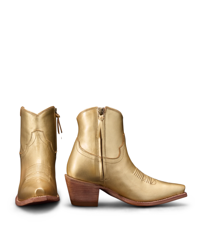 Two gold cowboy boots, one facing forward and the other showing the side, with engraved details and wooden heels.