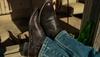 A person wearing blue jeans and dark brown boots rests their feet on a wooden surface outdoors, with a green glass bottle nearby and empty chairs in the background.