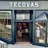 Exterior view of a Tecovas store with glass doors and windows displaying boots and clothing. Stairs are on the left side, and a neon "BOOTS" sign is visible inside.