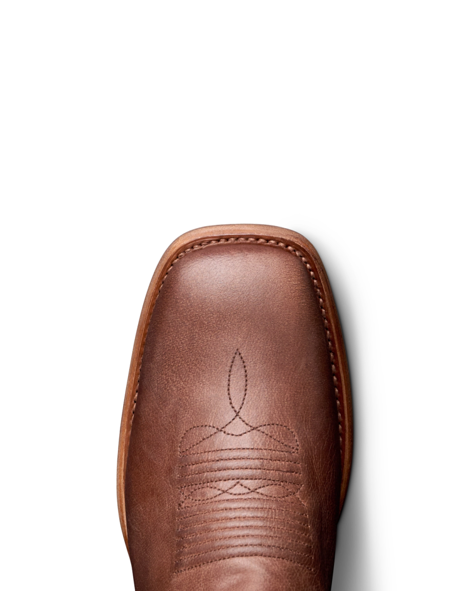 Close-up of a brown leather cowboy boot with decorative stitching on a black background.