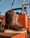 Brown leather boots with white soles are displayed outdoors on orange industrial equipment.