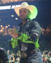 Man in a cowboy hat and rodeo outfit claps his hands at an indoor event, wearing a large belt buckle and a shirt with "Austin Gamblers" and sponsor logos.