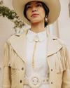 Woman in a white dress and fringed leather jacket wears a wide-brimmed hat outdoors.