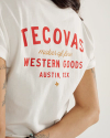 Person wearing a white T-shirt with red and gold text that reads "Tecovas Maker of Fine Western Goods Austin, Tex.