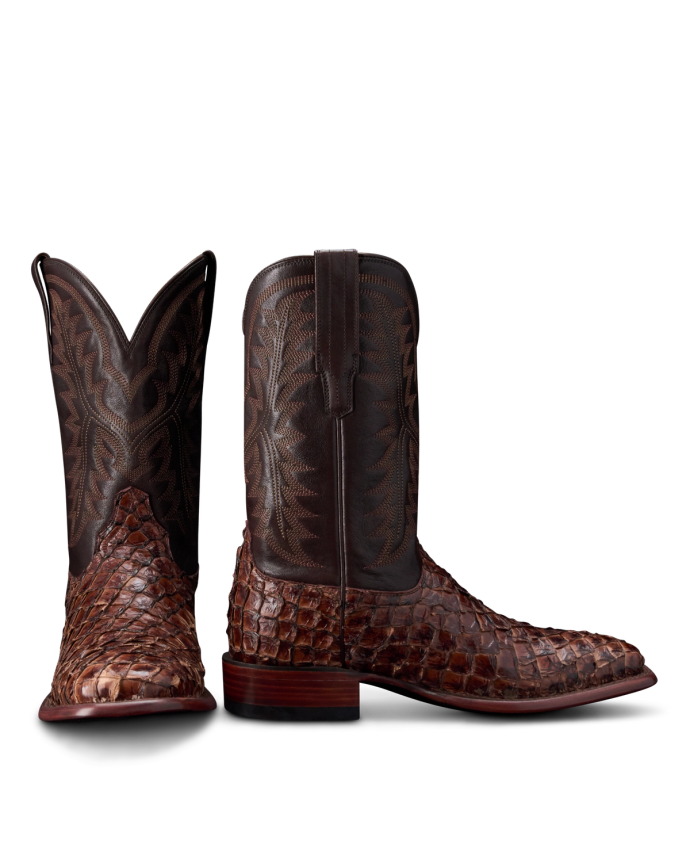 Two brown cowboy boots with intricate patterns and a textured, scaly surface. One boot is upright while the other is angled to display the design.