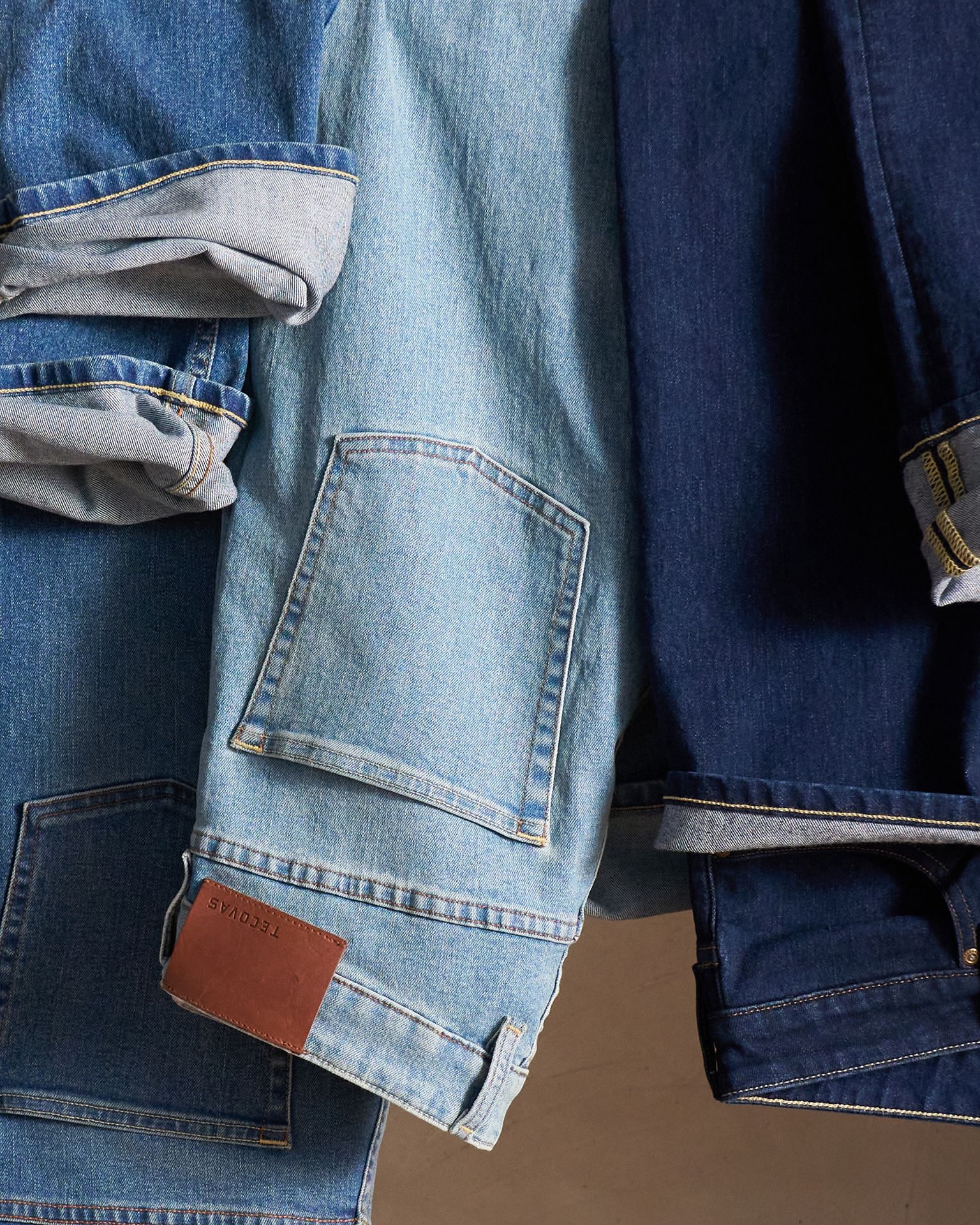 Three denim jackets in different shades of blue are hanging side by side, with visible pockets and stitching details.