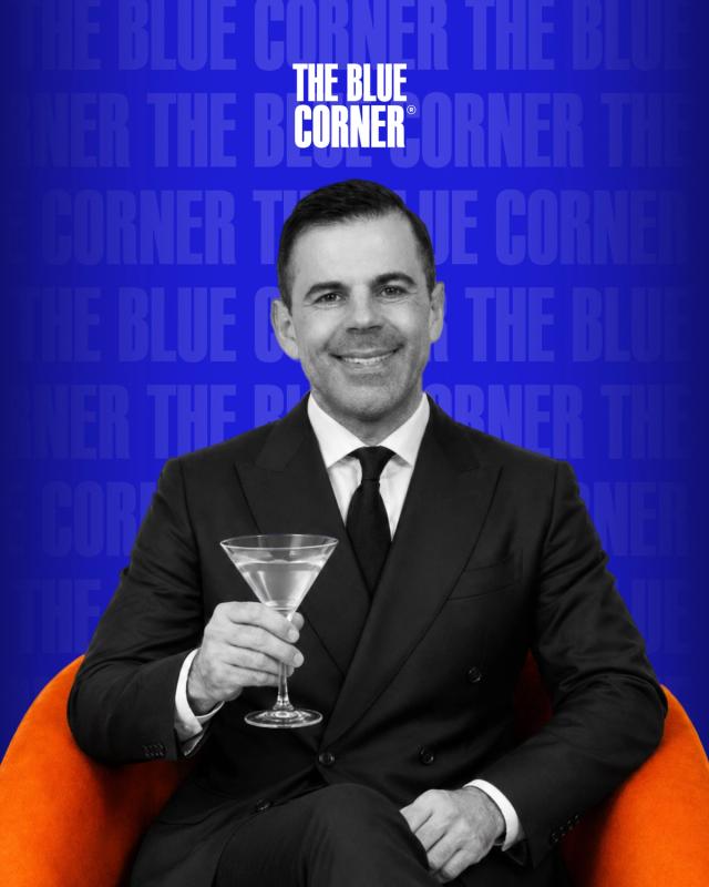 Agostino perrone del connaught bar seduto sulla poltrona arancione del podcast di the blue corner media mentre tiene un mano un cocktail martini e sorride