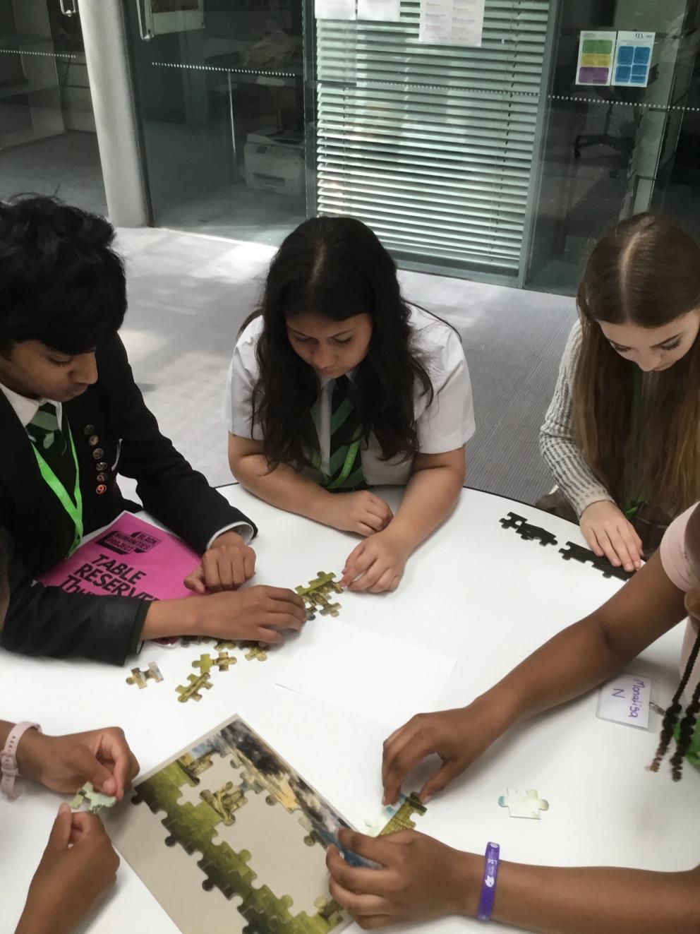 Students sitting round table completing a jigsaw puzzle.