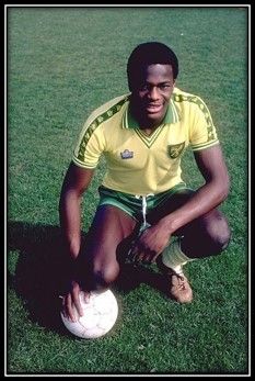 Justin Fashanu wearing a Norwich football kit and kneeling with one knee on a football.
