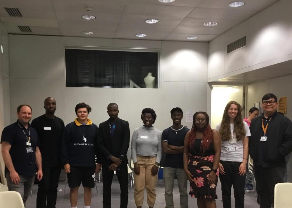 Group of 9 people standing in a row in a small seminar room