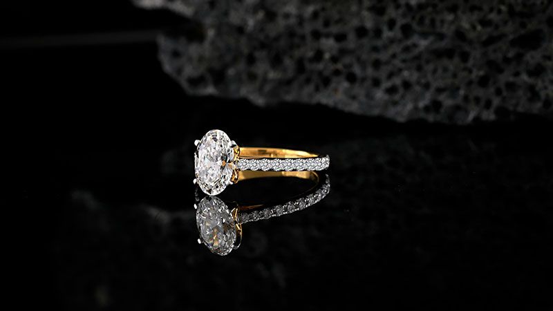 The design surrounds the main stone with small gems, enhancing moissanite’s brilliance.