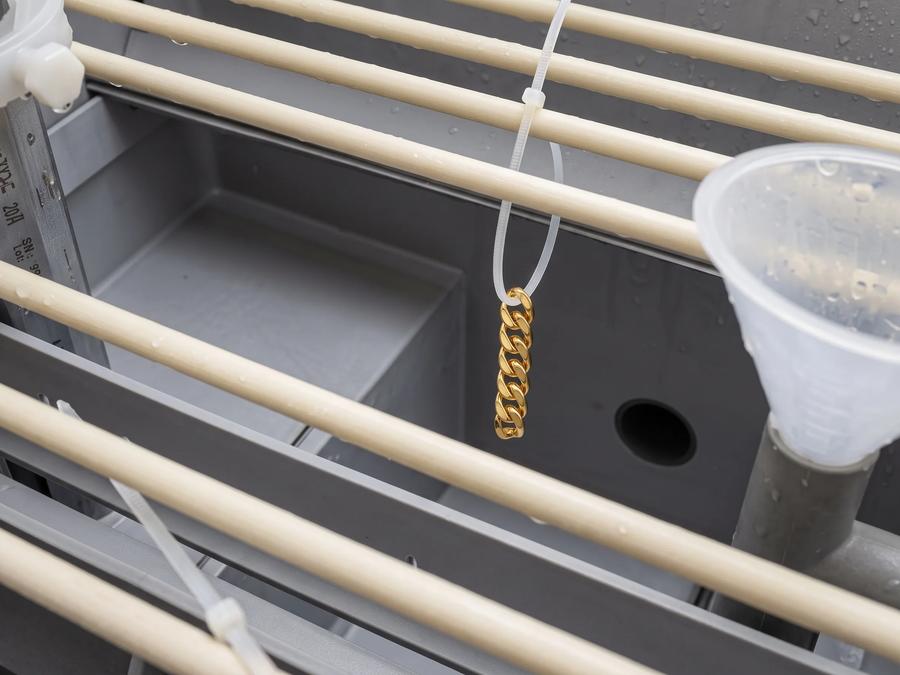 Gold Cuban chain undergoing plating durability testing above a process tank