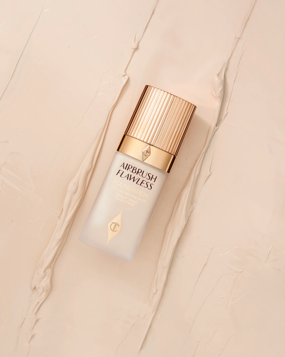 Charlotte Tilbury foundation bottle with gold cap laid on cream textured surface, beauty photography London