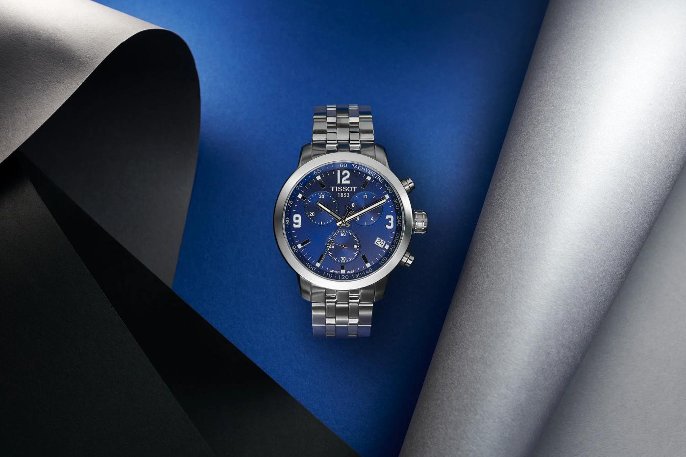 Tissot chronograph watch with blue dial and steel bracelet on layered blue and grey paper backdrop, luxury watch still life photography London