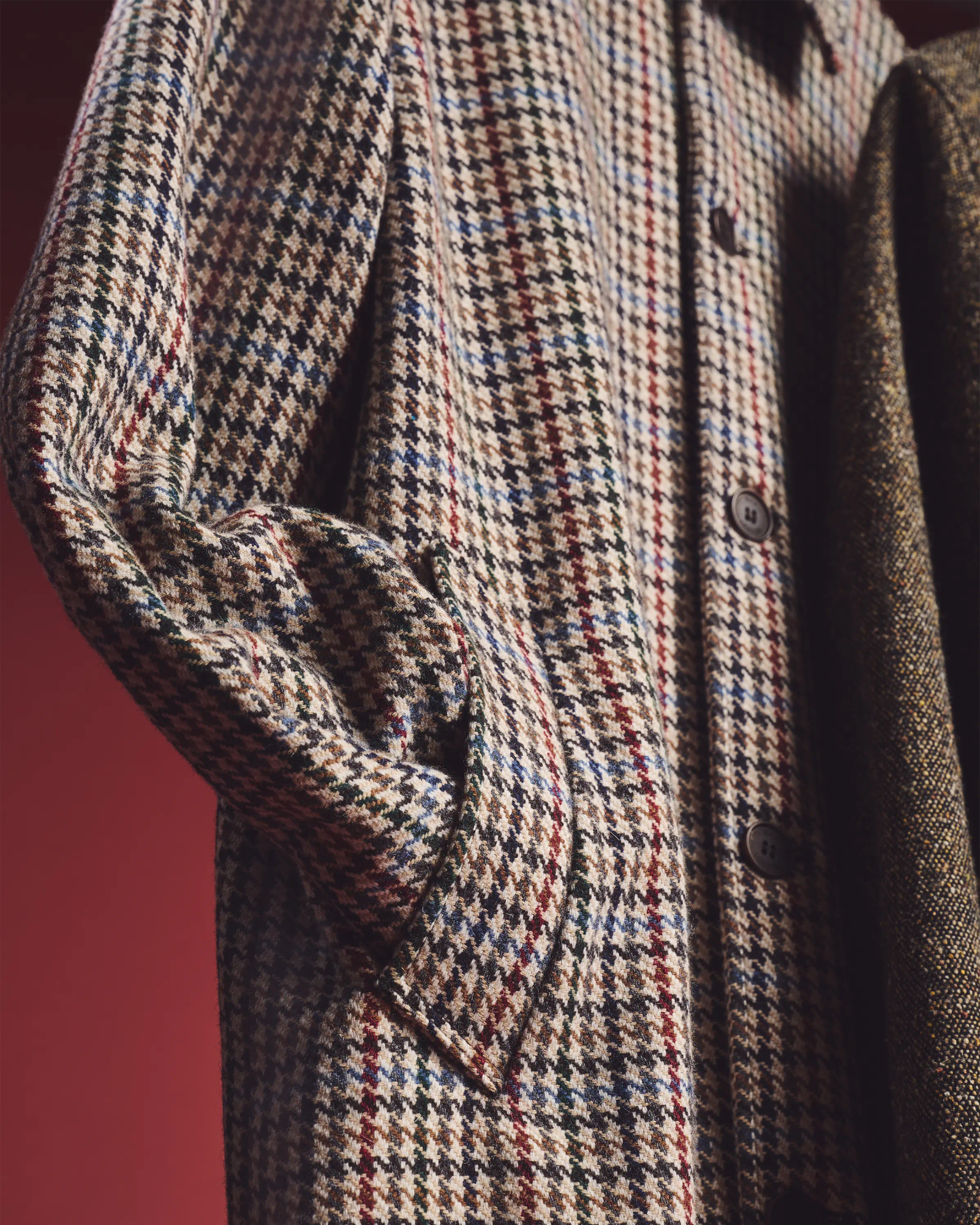close detail of Wax London houndstooth coat fabric with button placket against red backdrop, menswear product photography London