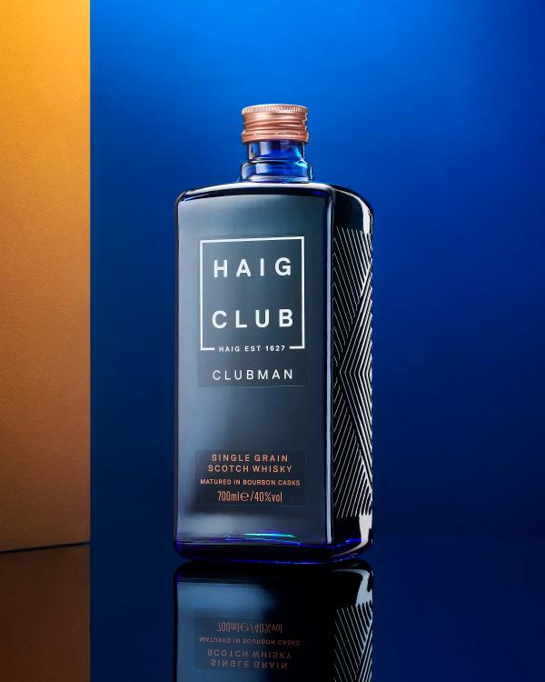 Haig Club Clubman whisky bottle against deep blue and gold backdrop with reflective surface, drinks photography London