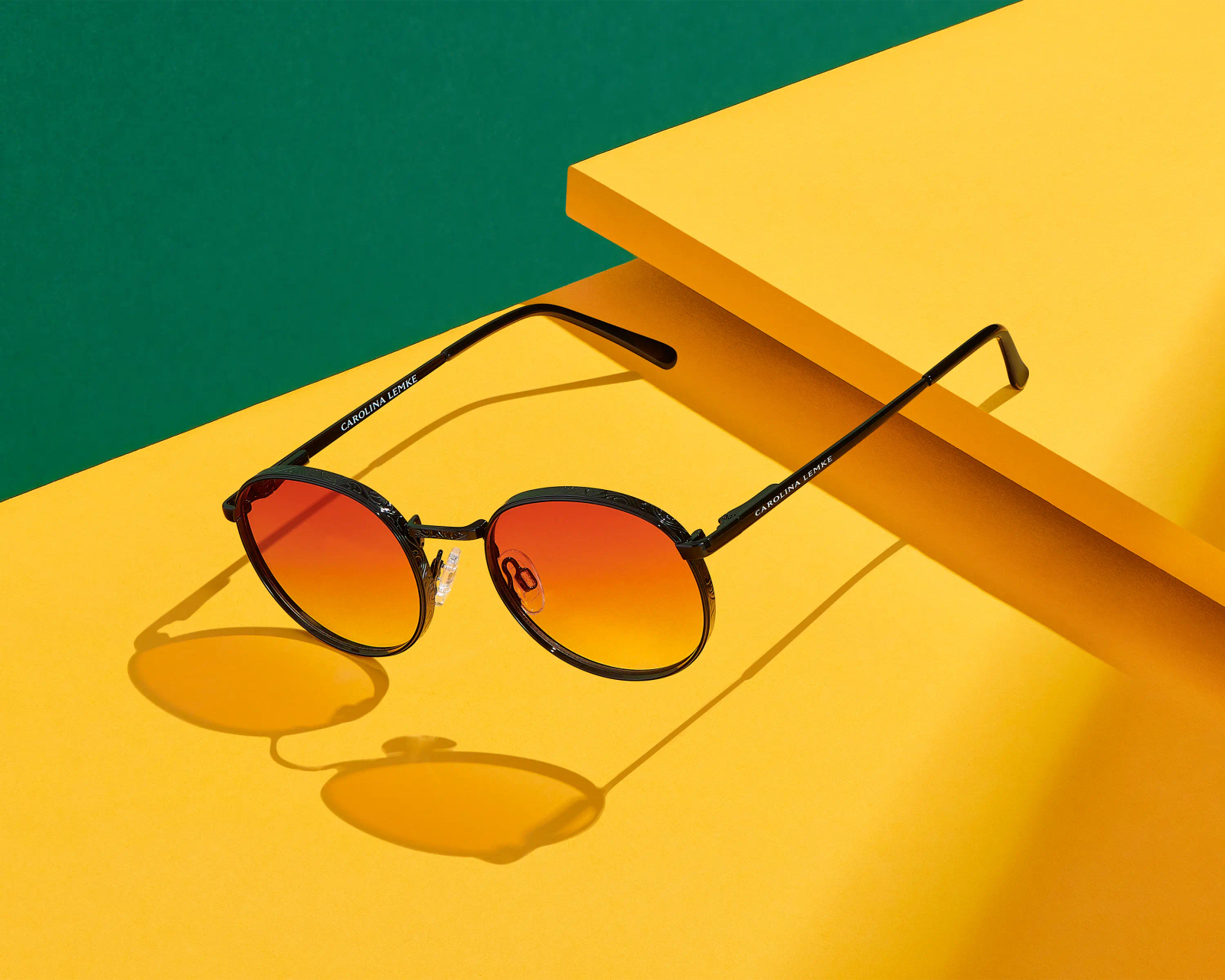 Carolina Lemke round sunglasses with amber gradient lenses on yellow geometric surface against green backdrop, eyewear photography London