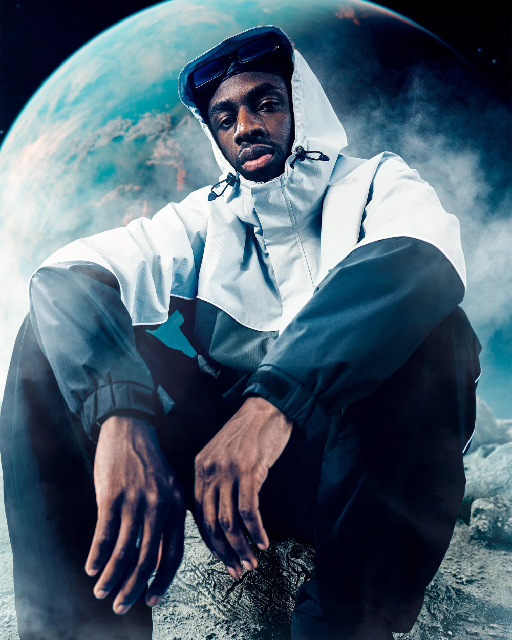 TBJZL seated on lunar surface in SDMN technical jacket with planet Earth backdrop, editorial fashion campaign photography London