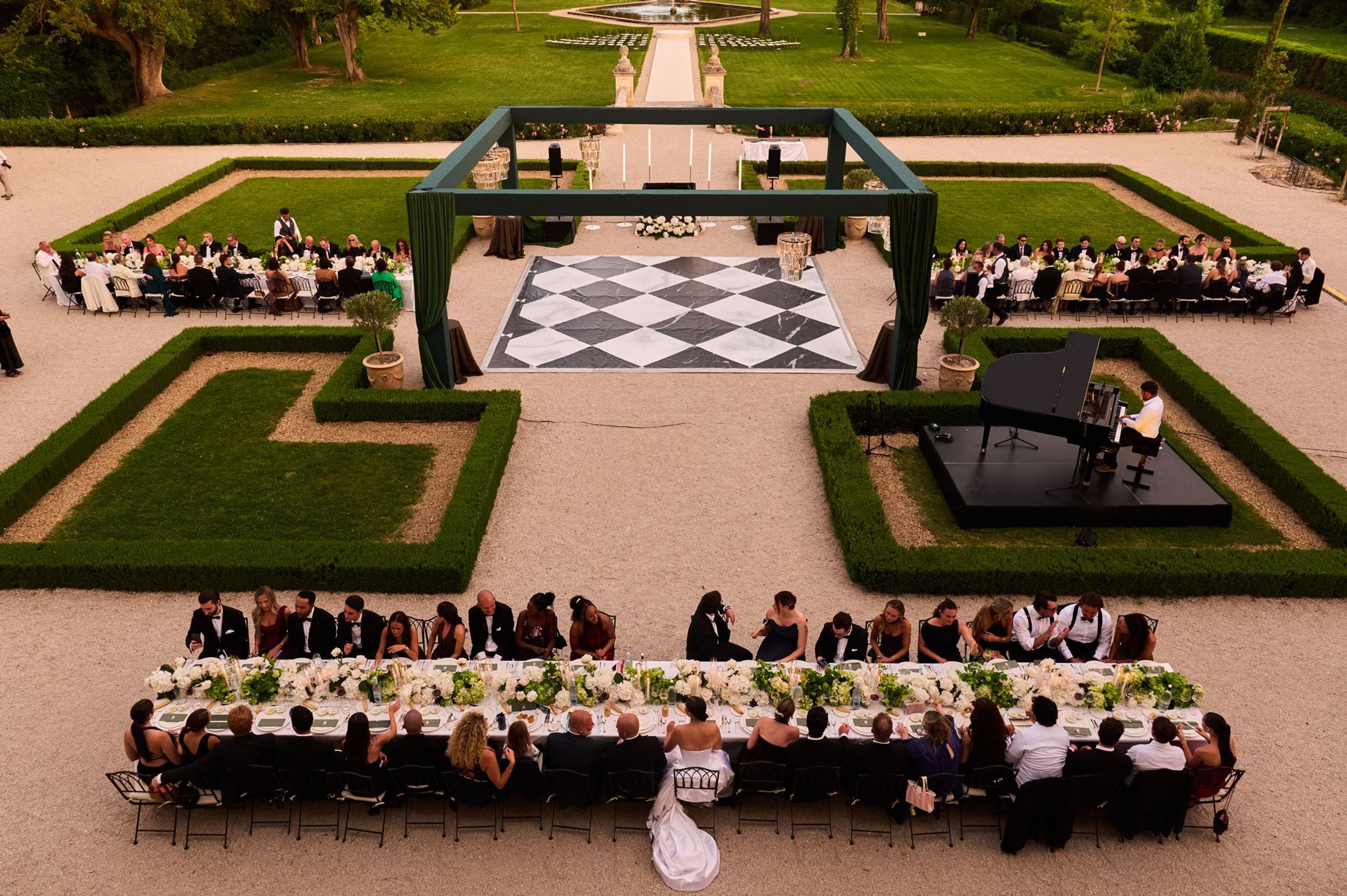 Long dinner tables in the French garden at Château de Tourreau, with a chequerboard dance floor beyond