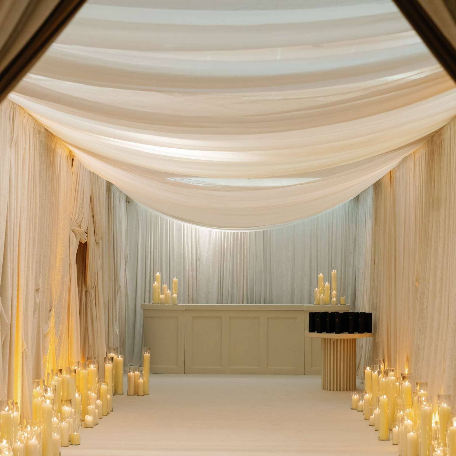 Ivory draping and candlelight along an aisle