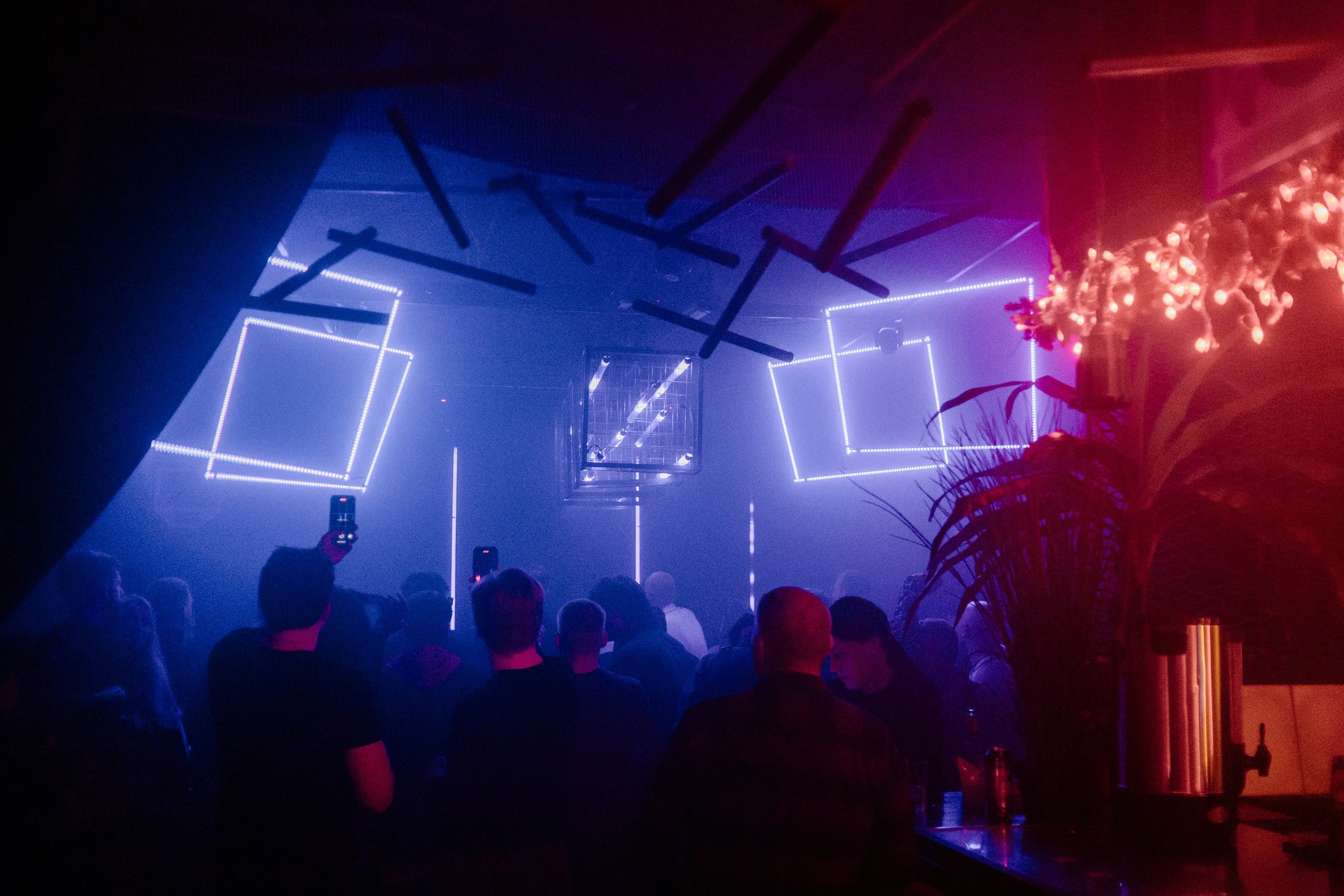 Stage lights cutting through haze above a crowd at an evening event