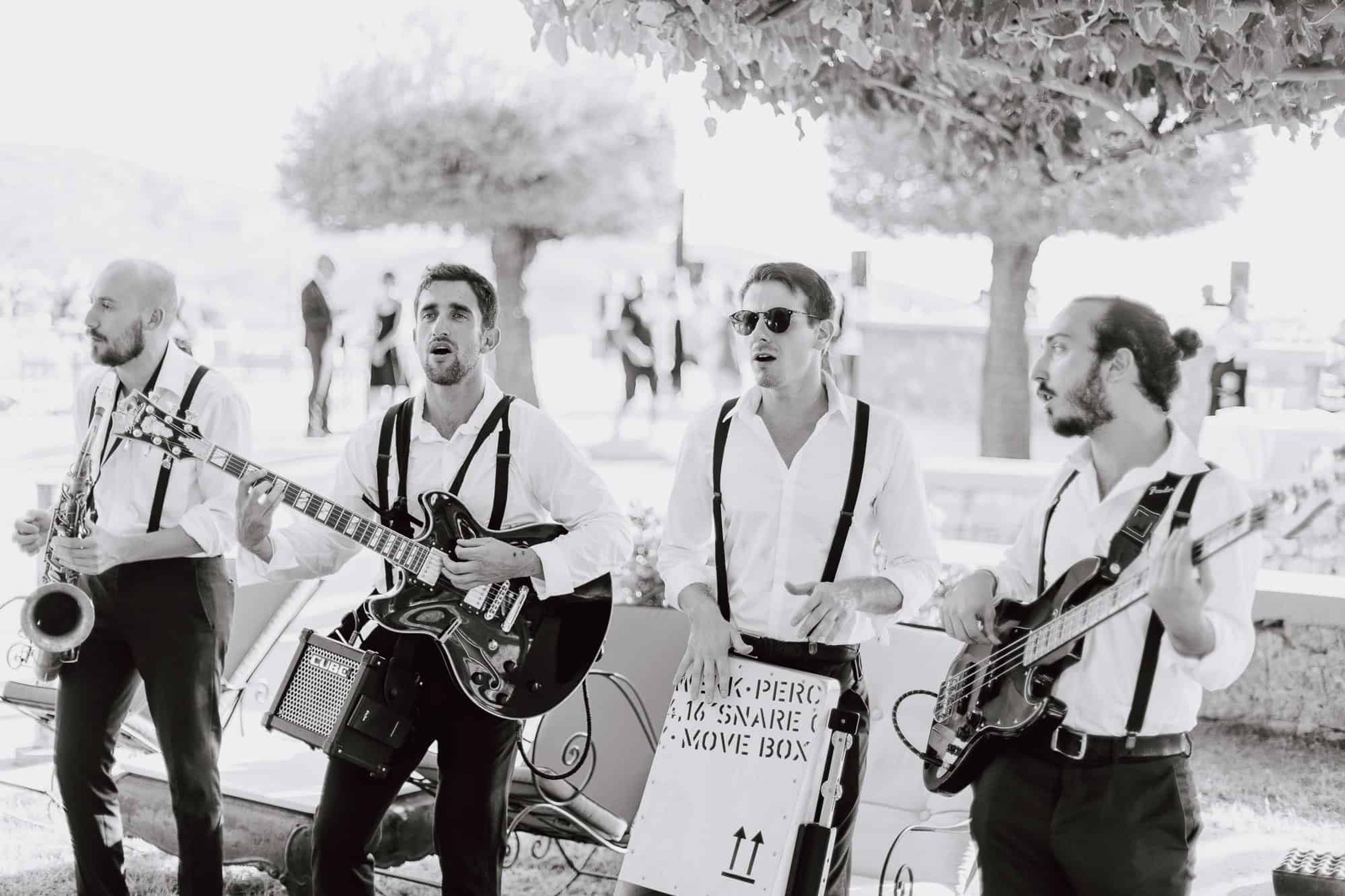 A band playing guitars and saxophone outdoors, in black and white