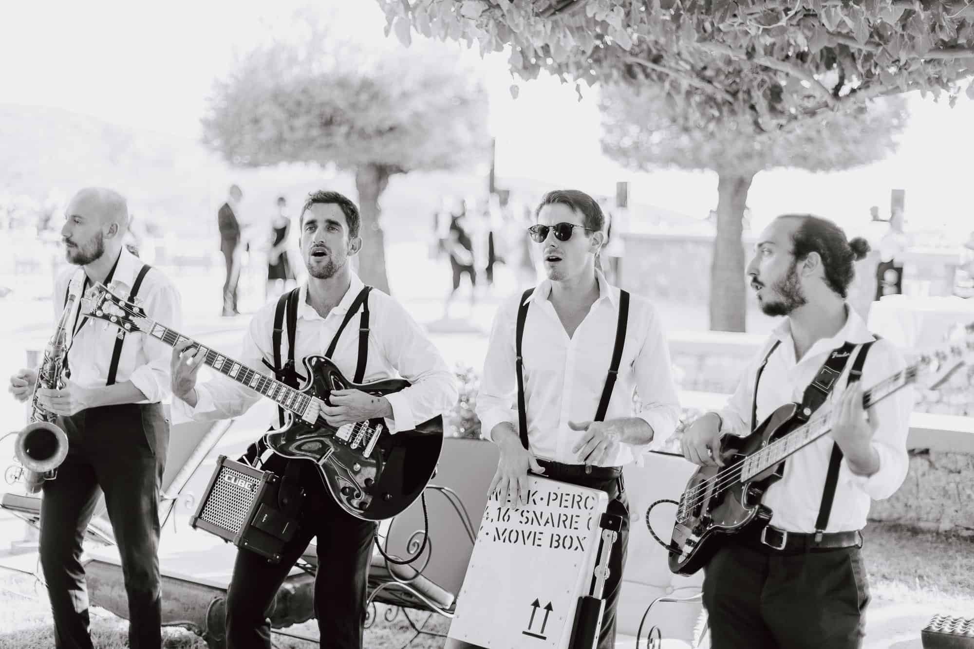 A band playing guitars and saxophone outdoors, in black and white