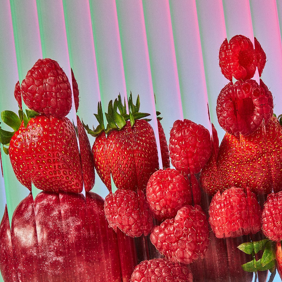 Red strawberries and raspberries stacked on top of each other photographed behind glass