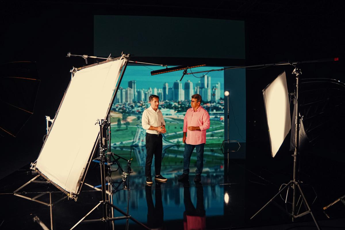 Duas pessoas em pé conversando diante do painel de LED exibindo o horizonte de uma cidade, com refletores de luz posicionados dos dois lados.