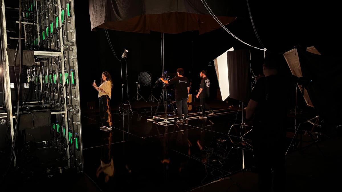 O painel de LED visto por trás, com os módulos acesos, e a cantora do outro lado do set