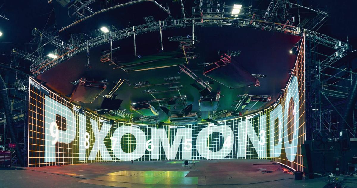 Um grande painel de led curvo, em um estúdio de alta tecnologia, com a palavra "pixomondo" destacada em letras brancas em negrito contra um fundo de grade colorido.