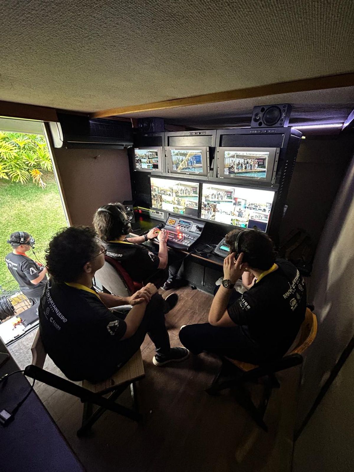 Operadores de headset sentados diante dos monitores e da mesa de corte da unidade móvel