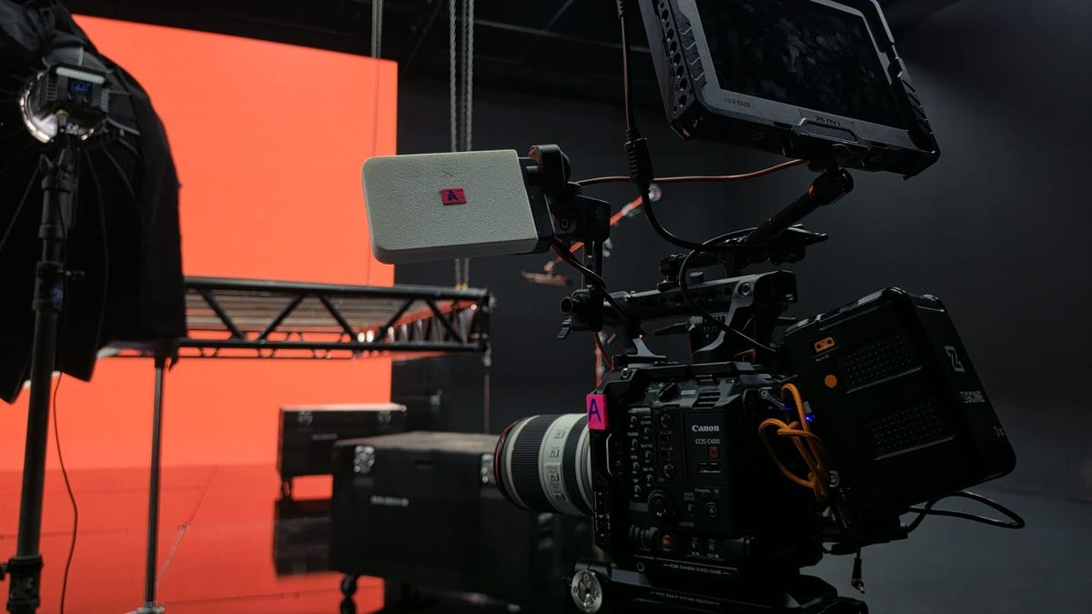 Câmera Canon EOS C400 montada com monitor e zoom branco no set, com o painel de LED laranja ao fundo