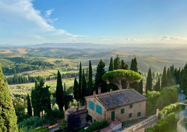 A stone farmhouse with blue shutters among cypress trees, overlooking the rolling hills of Tuscany