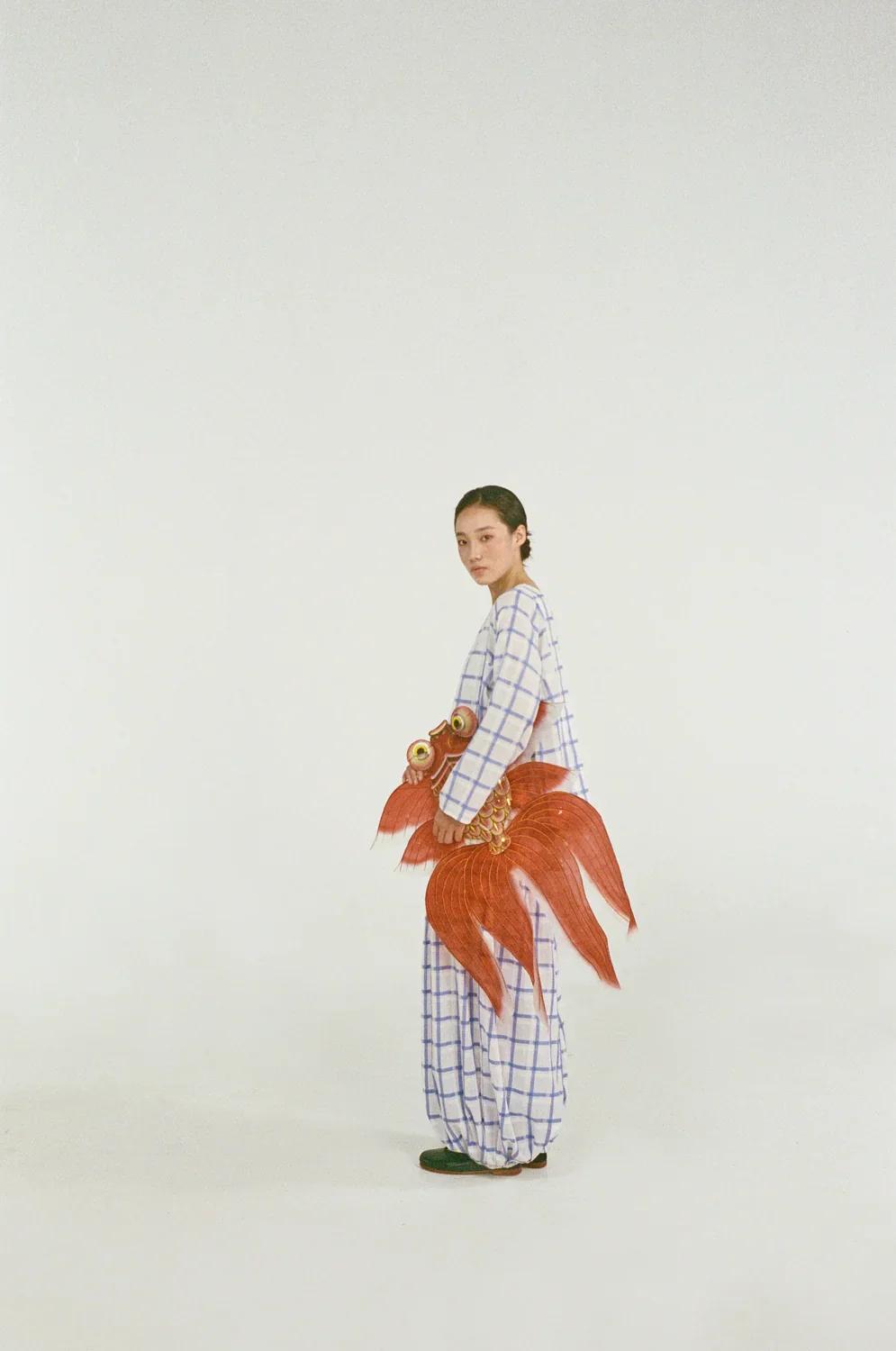 Model in a blue-and-white checked Unisecon set holding a red goldfish-shaped kite