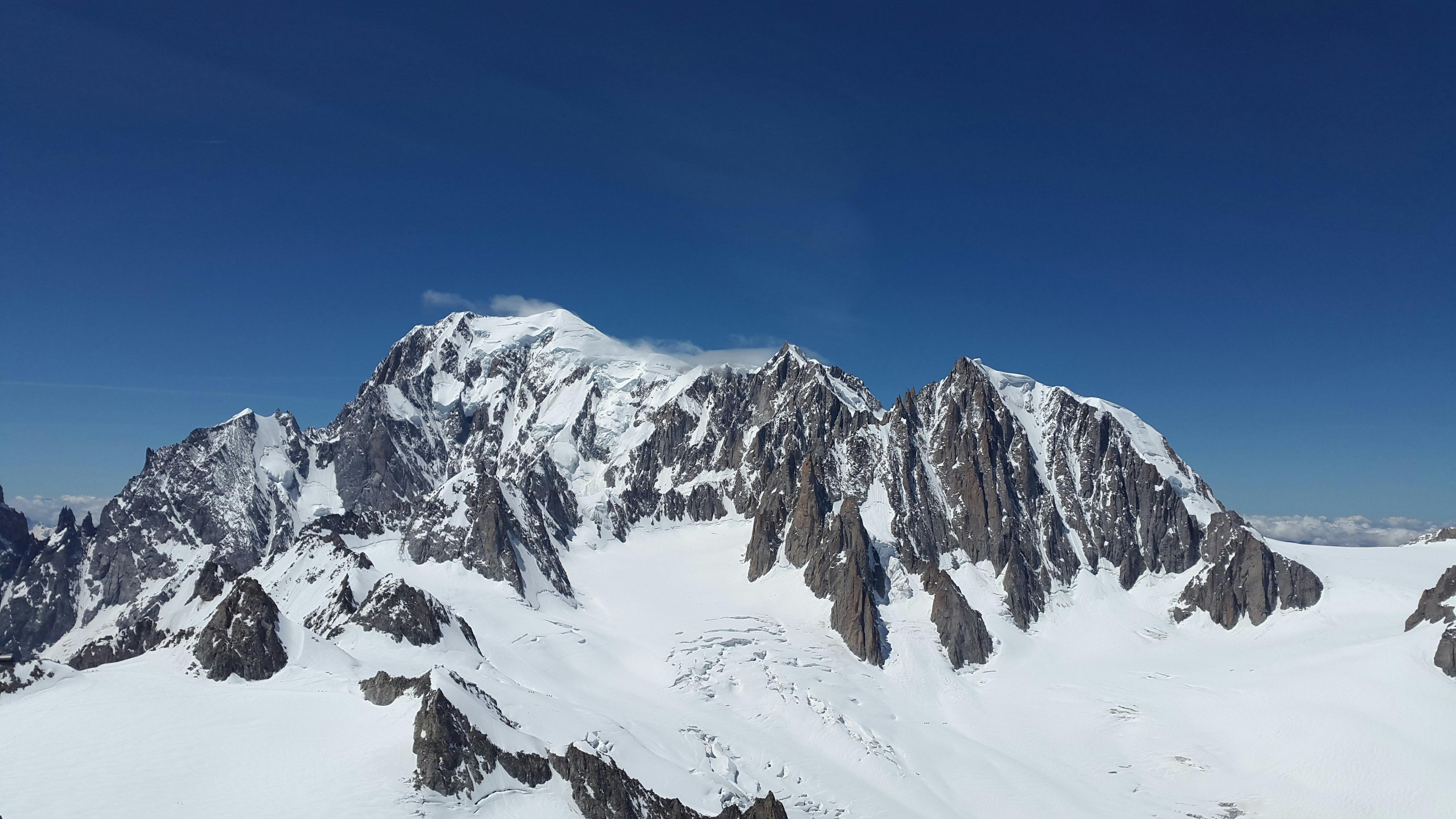 Bilde av noen fjell med masse snø. Blå himmel i bakgrunnen.