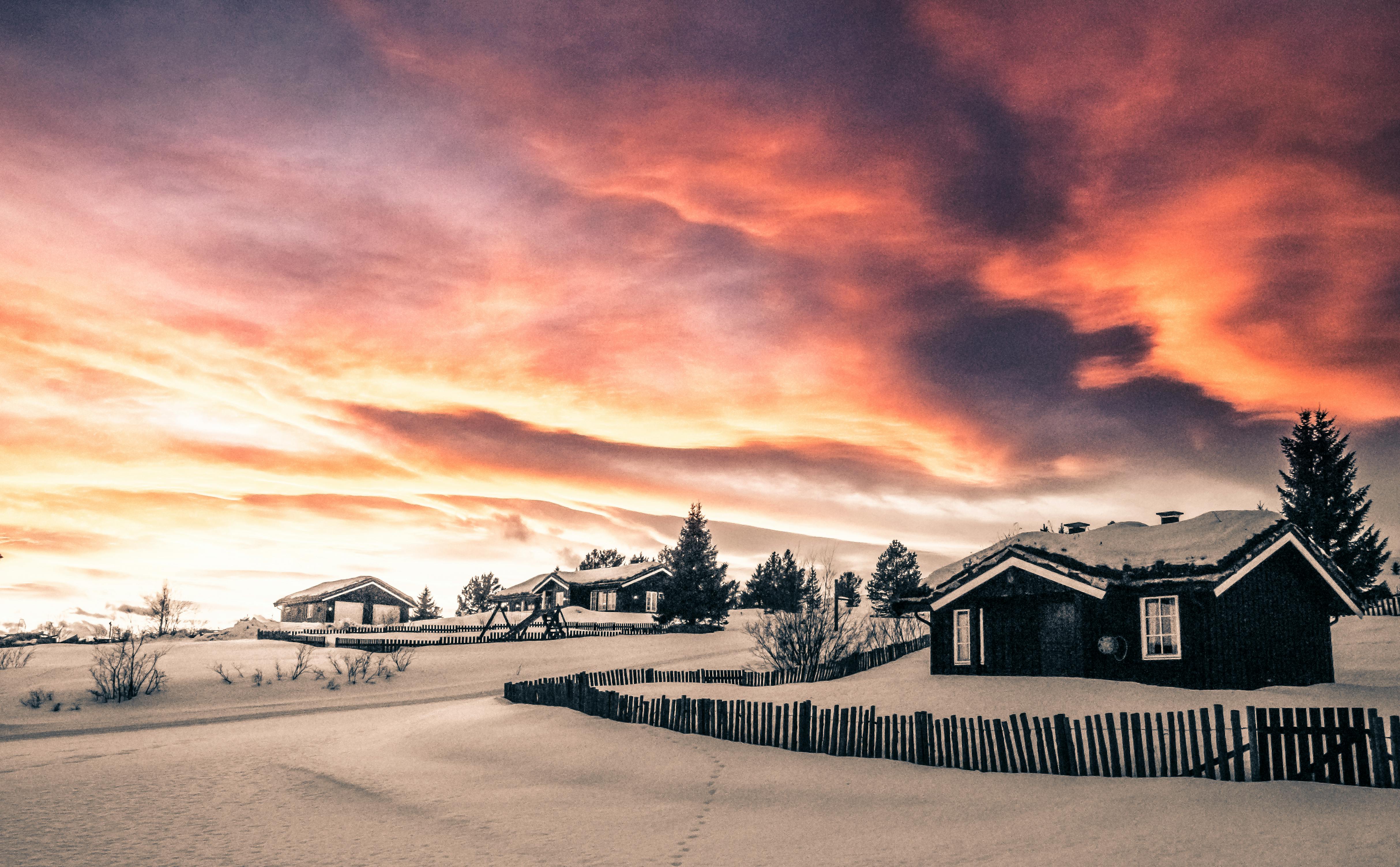 Bilde av noen hytter dekket av snø med skyer og sol i bakgrunnen.