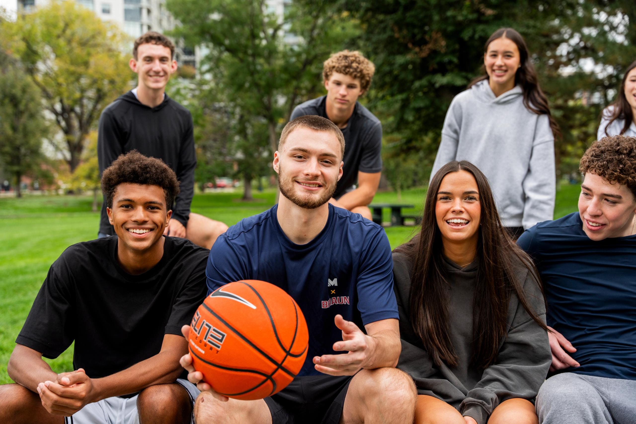 Christian Braun sitting with a group of young people on an outdoor basketball court.