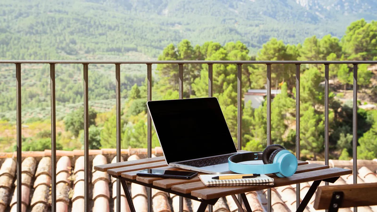 A laptop and notebook on a balcony table overlooking green hills